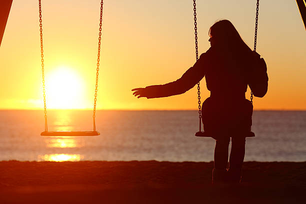 Person on a swing at sunset, second empty swing beside them